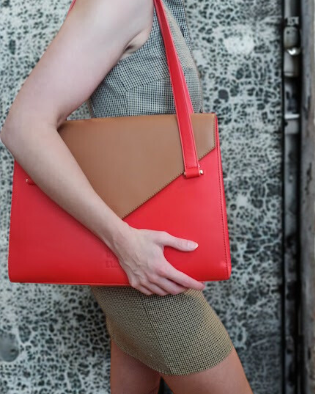 Person holding a red bag with brown flap against a patterned background